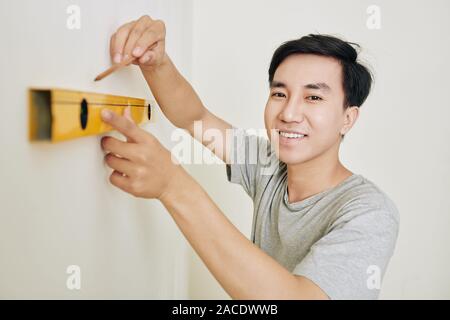 Cheerful young Asian man drawing line when measuring wall in his new apartment Stock Photo