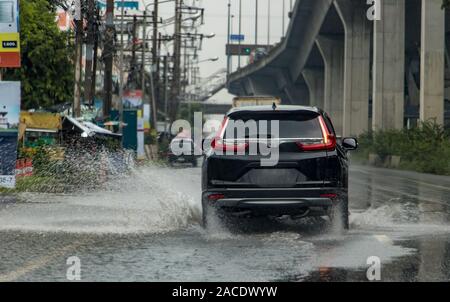 The car ride through a puddle from which water is sprayed. Traffic in the rain season, Bangkok, Thailand. Stock Photo