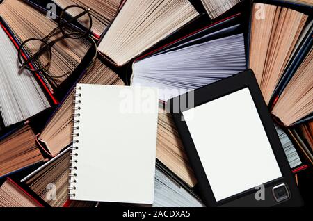 The e-book with a white screen lies on the open multi-colored books that lie on a dark background, close-up Stock Photo