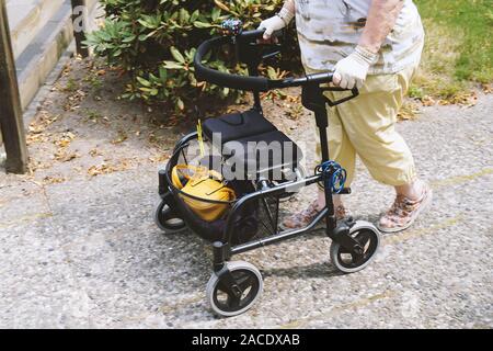 elderly woman walking outside with rollator or wheeled walker - authentic real people concept Stock Photo