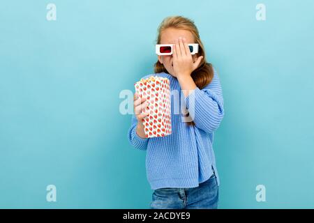 attractive girl in movie glasses is holding popcorn in her hands on a light blue wall. Stock Photo