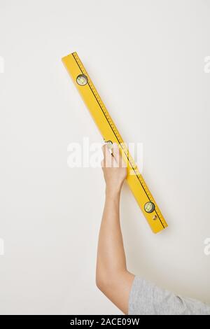 Hand of repairman holding spirit level against white wall in new apartment Stock Photo