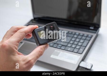 Action camera in hand. Laptop in background. Concept of transferring and storing data from a camera to a computer. Stock Photo