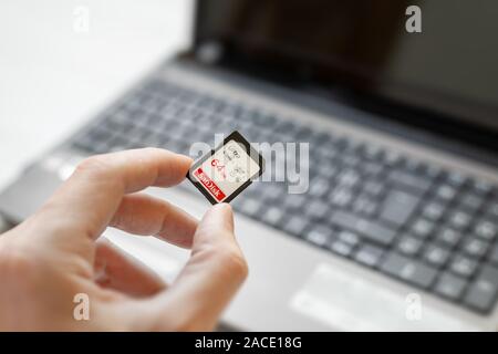 Hand holding 64 GB SD card above laptop computer. Concept of transferring photos and videos from a card to a computer Stock Photo