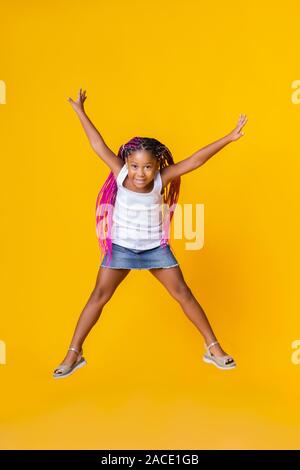 Cute little afro girl jumping over yellow studio background Stock Photo