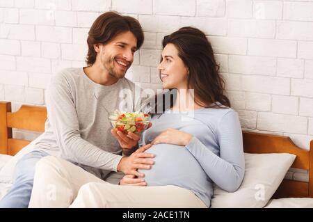 Loving husband feeding his pregnant wife with fresh vegetable salad Stock Photo