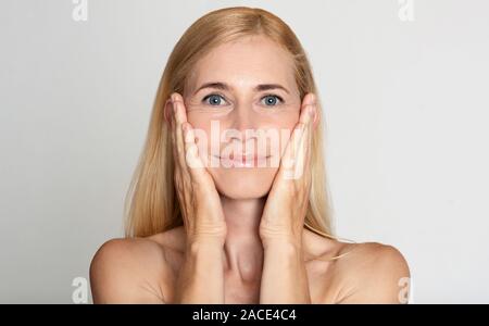 Anti aging treatment. Middle-aged woman touching cheeks Stock Photo