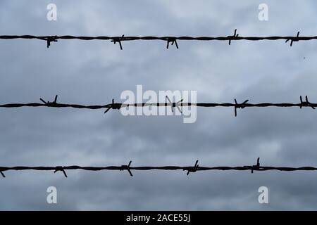 Three rows of barbed wire in front of the dark and cloudy sky - security concept Stock Photo