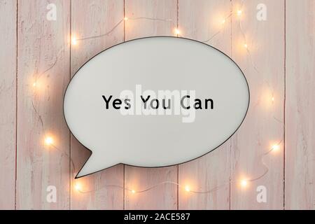 Yes You Can written on speech bubble, surrounded by bright lights on pink wooden background Stock Photo