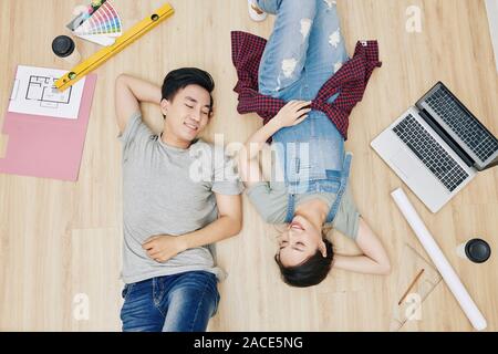 Happy tired young Vietnamese couple resting on the floor after planning design of new apartment, view from above Stock Photo