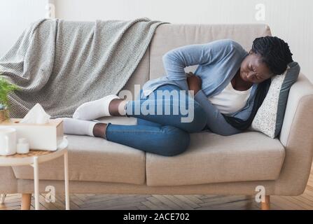 Sick Afro Girl Lying On Couch Suffering From Abdominal Pain Stock Photo