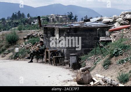 11th August 1993 During the Siege of Sarajevo: a Bosnian-Serb soldier relaxes outside his bunker on Mount Trebevic, above Sarajevo. A belt of spent M2 Browning .50 calibre cartridges hang below a Serbian cross symbol on the front of the hut. Stock Photo
