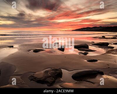 Charmouth, Dorset, UK. 2nd December 2019. UK Weather: Spectacular colours are reflected in the wet sand at low tide as the sun sets over the beach at the coastal resort of Charmouth.  The popular beach is almost deserted as the sun drops below the horizon towards Lyme Regis.     Credit: Celia McMahon/Alamy Live News. Stock Photo