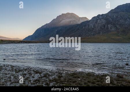 Morning light on snow capped peak of Tryfan from banks of Lake or Llyn Idwal. Snowdonia national Park, Gwynedd, Wales, UK. landscape. Stock Photo