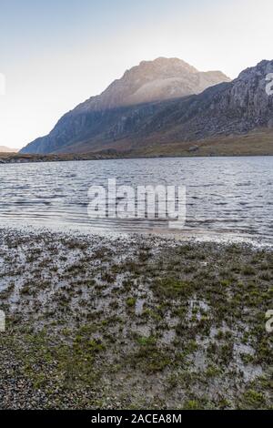 Morning light on snow capped peak of Tryfan from banks of Lake or Llyn Idwal. Snowdonia national Park, Gwynedd, Wales, UK. portrait. Stock Photo