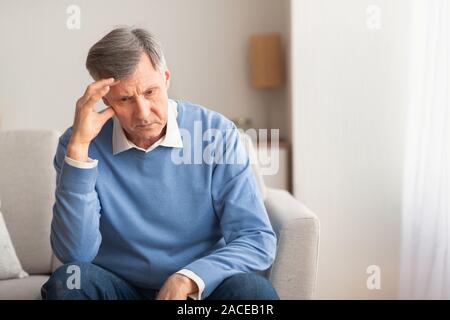 Elderly Man Thinking About Loneliness Sitting On Couch At Home Stock Photo