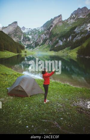 Woman taking photograph by tent near Seealpsee lake in Appenzell Alps, Switzerland Stock Photo