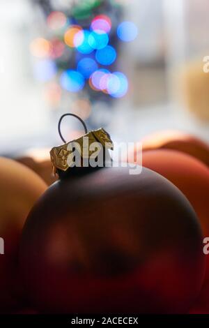 Close-up of matte bronze orange christmas balls in front of blurred bokeh christmas lights in blue, orange, red and green Stock Photo