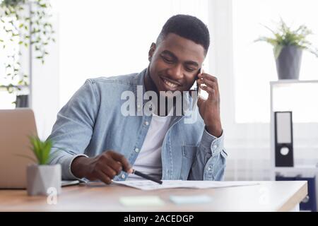 African businessman talking with companion on phone and checking financial reports Stock Photo