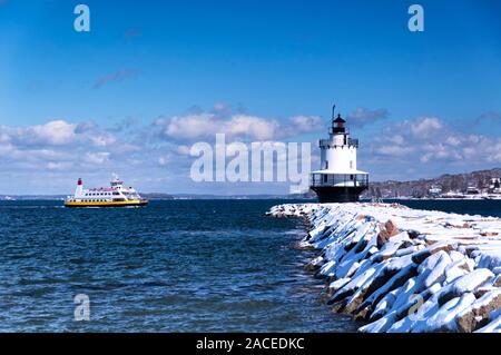 A passenger ferry traveling near the snow covered spring point ledge lighthouse in portland maine on a blue sky winter day. Stock Photo