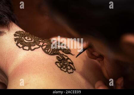 Drawing process of henna mehendi ornament on woman's back. Tattoo painting henna Stock Photo
