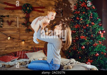 Young mother playing with baby near Christmas tree Stock Photo