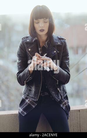 Portrait of a young woman with rock jacket smoking cigarette.