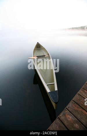 A sleek canoe tied to a dock on a tranquil pond in Maine. Stock Photo