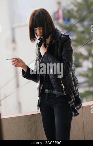 Portrait of a young woman with rock jacket smoking cigarette. Stock Photo