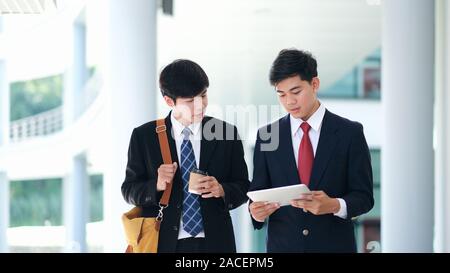 Business people walking and talking in the office building. Two confident business partners walking down in office building and talking while taking c Stock Photo