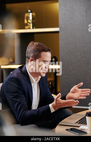 Young confident entrepreneur wearing earbuds when video calling business partner and discussing current work Stock Photo