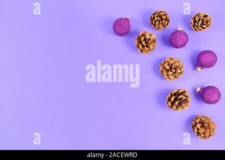 Seasonal Christmas flat lay with fir cones and gittering tree baubles on right side and empty purple copy space on left side on light purple backgroun Stock Photo