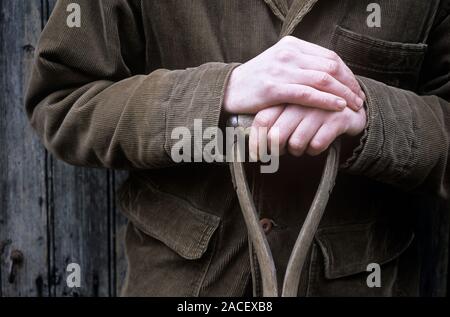Gardener's hands resting on the handle of a fork or spade. Stock Photo