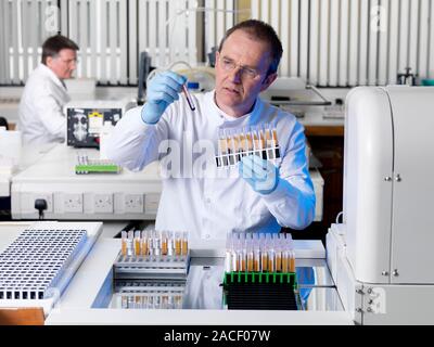 Blood typing. Technician preparing samples of donated blood for analysis. The samples will be tested automatically by a blood grouping analyser (right Stock Photo