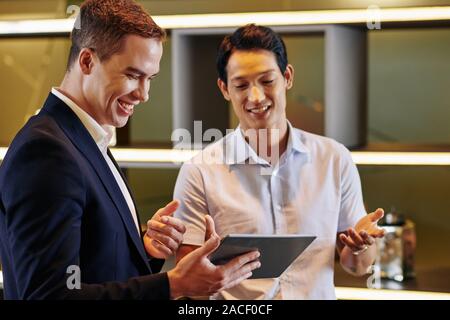 Cheerful friendly coworkers discussing new mobile application on tablet computer at meeting Stock Photo