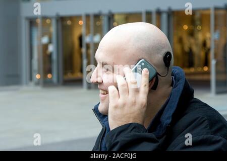 This is a real situation. Image not to be used in a defamatory context. Cochlea implant. Man with a cochlea implant using his mobile phone. A cochlea Stock Photo