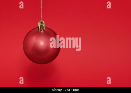 Red Christmas bauble hanging from gold string isolated against a red background, with copy space Stock Photo