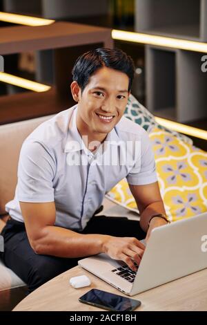Handsome young Vietnamese woman working on laptop when sitting at cafe in local cafe Stock Photo
