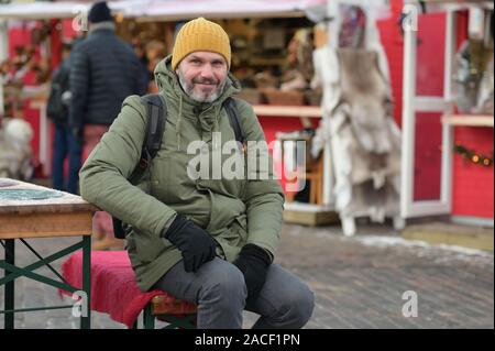 Mature bearded man with backpack resting at the outdoor table on the Christmas market on Kauppatori square in Helsinki, Finland Stock Photo