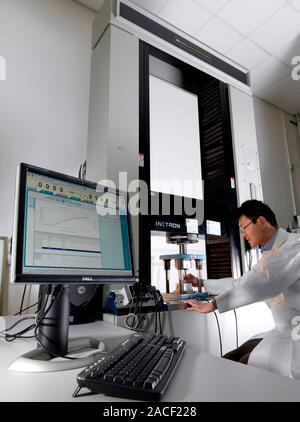 Materials testing. Technician testing an object in a typical static test machine (centre, large vertical). Static testing involves subjecting a materi Stock Photo