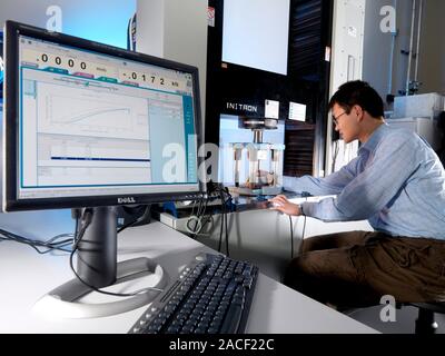 Materials testing. Technician testing an object in a typical static test machine (centre, large vertical). Static testing involves subjecting a materi Stock Photo