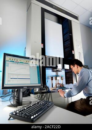 Materials testing. Technician testing an object in a typical static test machine (centre, large vertical). Static testing involves subjecting a materi Stock Photo