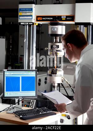 Materials testing. Technician testing an object in a typical mechanical fatigue test machine (centre). In materials science, fatigue is the progressiv Stock Photo