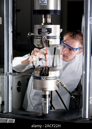 Materials testing. Technician testing an object in a typical mechanical fatigue test machine (centre). In materials science, fatigue is the progressiv Stock Photo