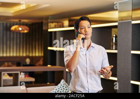 Handsome young Asian man gesturing when talking on phone with business partner Stock Photo