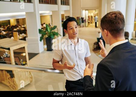 Handsome serious Vietnamese entrepreneur listening to business partner talking talking about project and showing three fingers Stock Photo