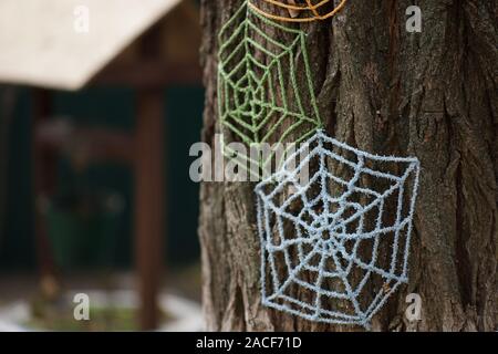 Blue and green knitted cobwebs on a tree trunk close-up. Stock Photo
