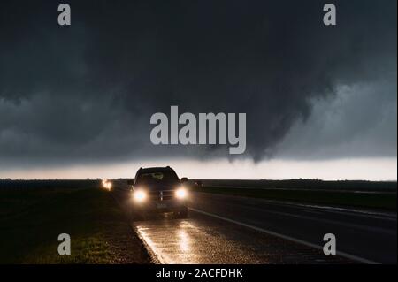 Tornado forming over road. Motorists stopped on a road as a developing tornado moves overhead, right-to-left, darkening the sky. A tornado is a violen Stock Photo