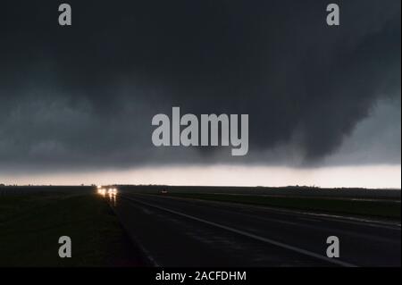Tornado forming over road. Motorists (centre left) stopped on a road as a developing tornado moves overhead, right-to-left, darkening the sky. A torna Stock Photo