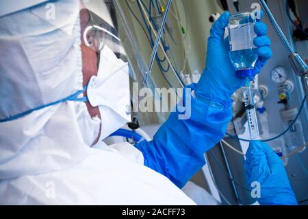 Infection prevention in intensive care. Intensive care unit (ICU) nurse filling a syringe whilst wearing a virus protection suit. This suit is designe Stock Photo